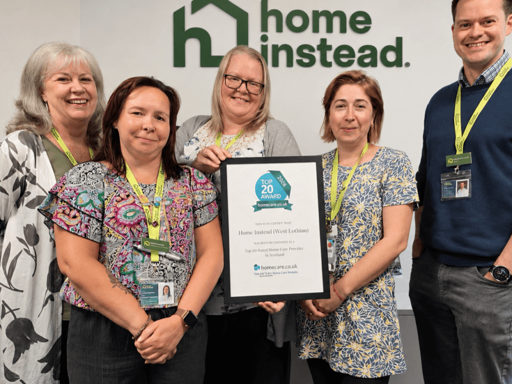 Five smiling people holding a framed award in front of a "Home Instead" logo on a wall. - Home Instead