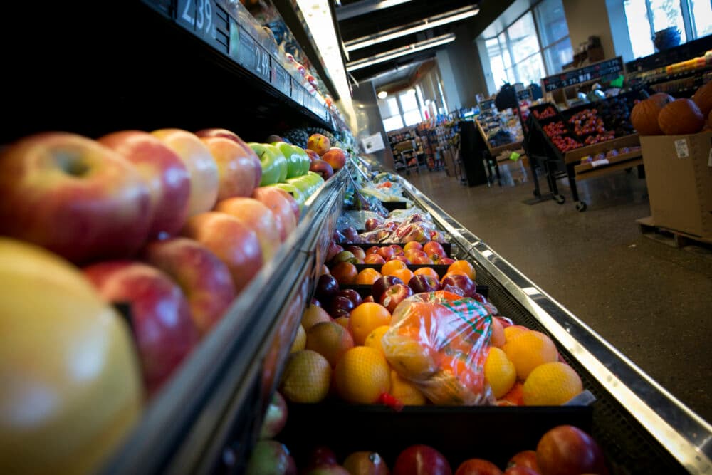 A shot looking along the fruit and vegetable counter in a supermarket with apples and citrus fruits in the foreground and racks with other fruit and vegetables in the background