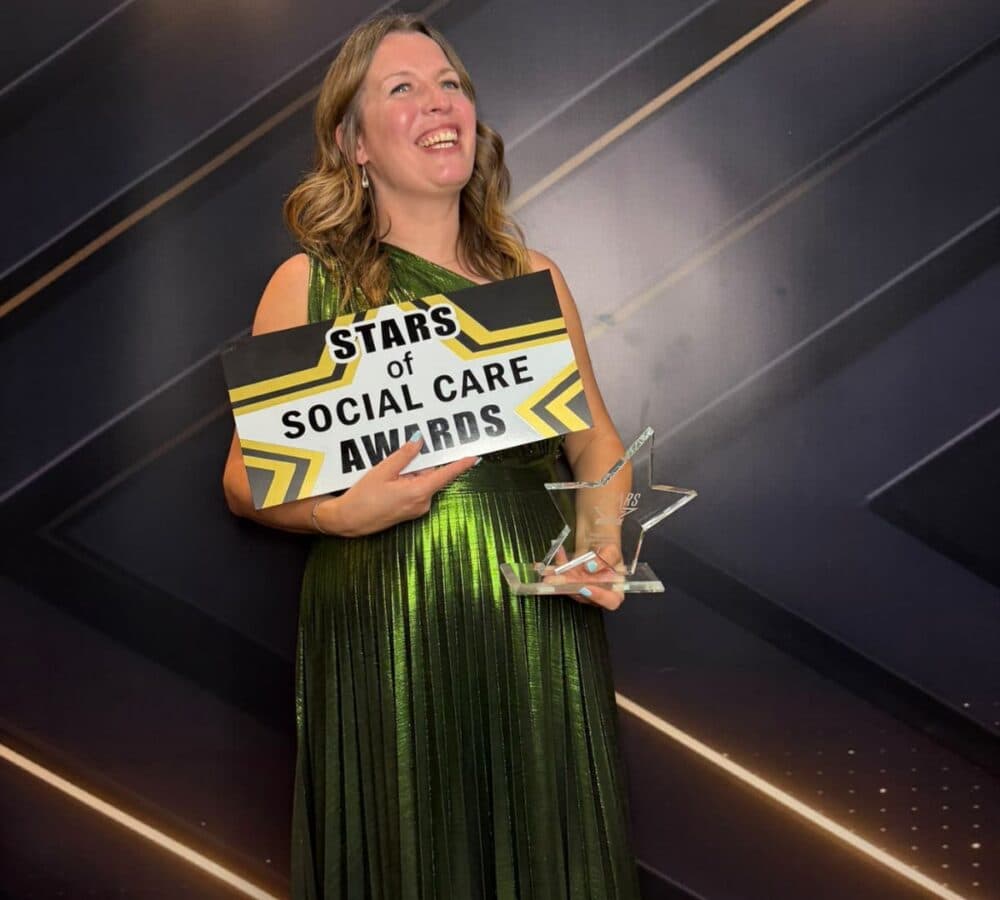 Woman in a shiny green dress holding a "Stars of Social Care Awards" sign and a star-shaped trophy. - Home Instead