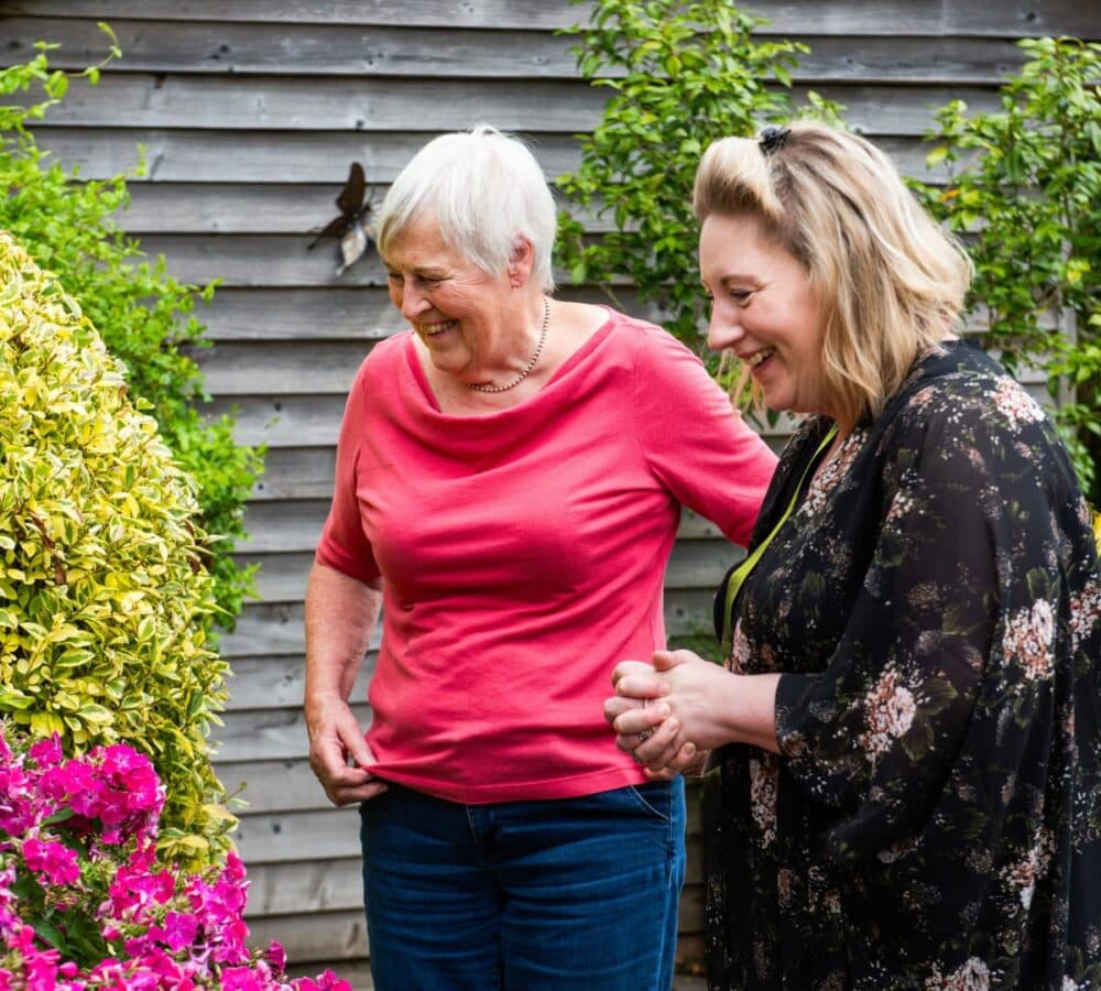 Two women looking at flowers in the garden both happy and smiling