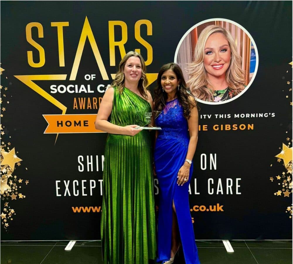 Two women in evening dresses pose with an award in front of a "Stars of Social Care Awards" backdrop. - Home Instead