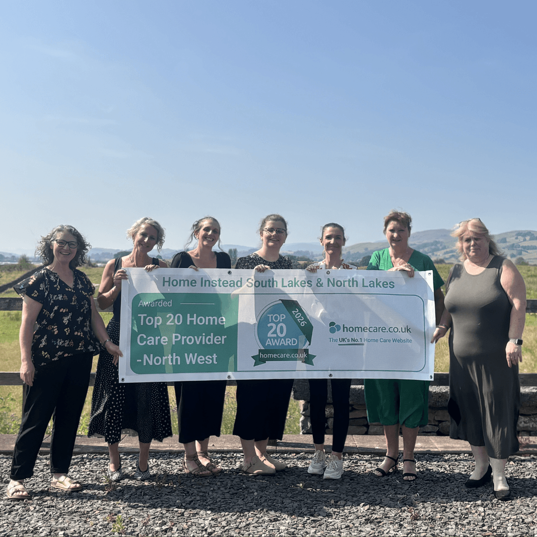 Seven women stand outdoors holding a banner for a top 20 home care provider in the North West region. - Home Instead