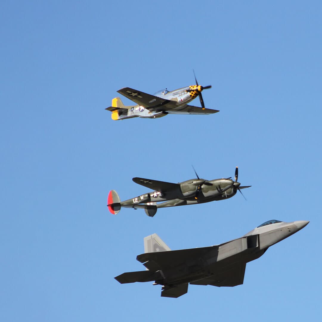 Three vintage military aircraft in flight against a clear blue sky. - Home Instead