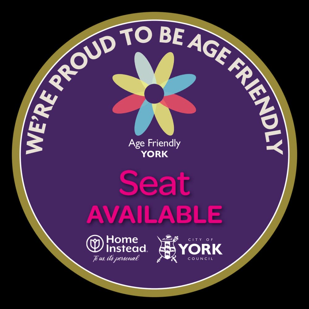 A round sign with "We're Proud to Be Age Friendly" and "Seat Available" text, featuring logos of Home Instead and York Council. - Home Instead