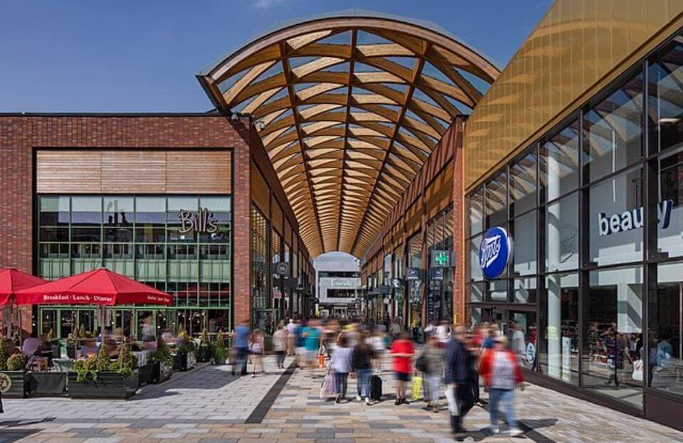 Open-air shopping center with a wooden roof, bustling with people, and lined with shops and restaurants on both sides. - Home Instead