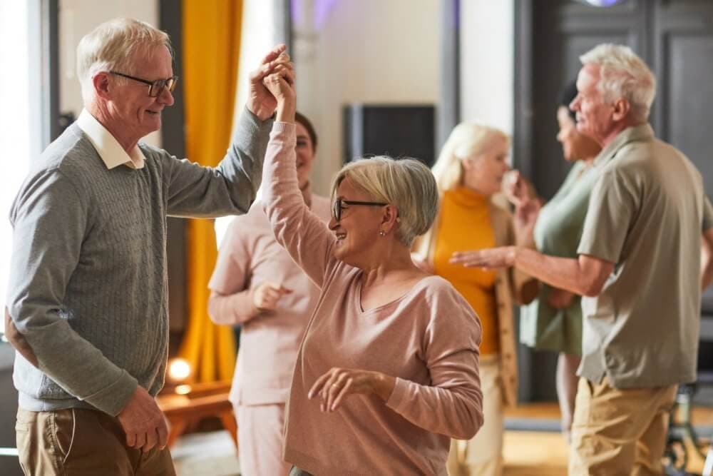 Elderly couples dancing and socializing in a warmly lit room. - Home Instead