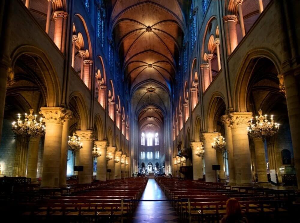 Interior of a grand cathedral with high ceilings, arched columns, stained glass windows, and rows of pews. - Home Instead