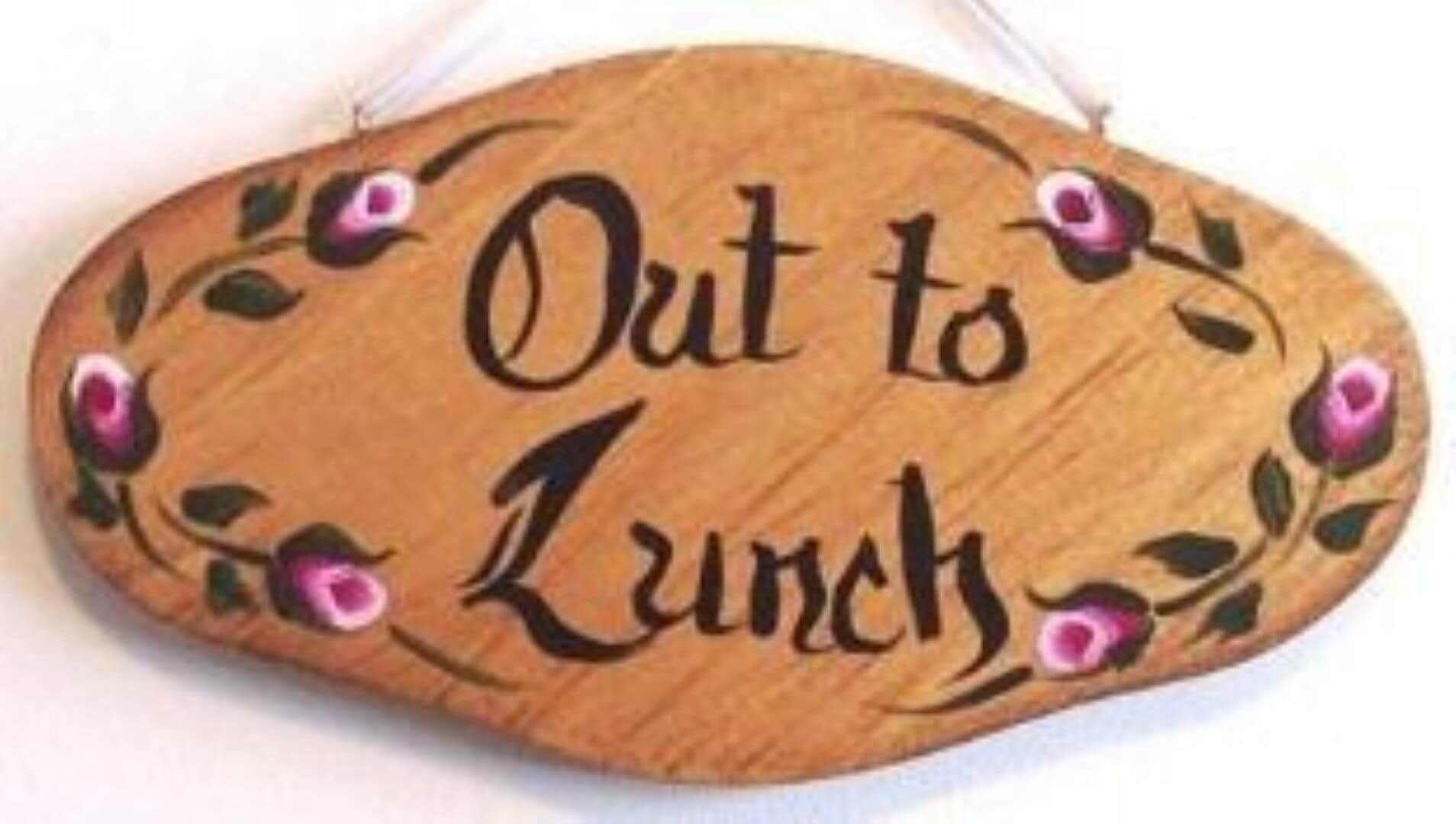 Wooden sign with "Out to Lunch" written in stylized black lettering, decorated with painted flowers along the edges. - Home Instead