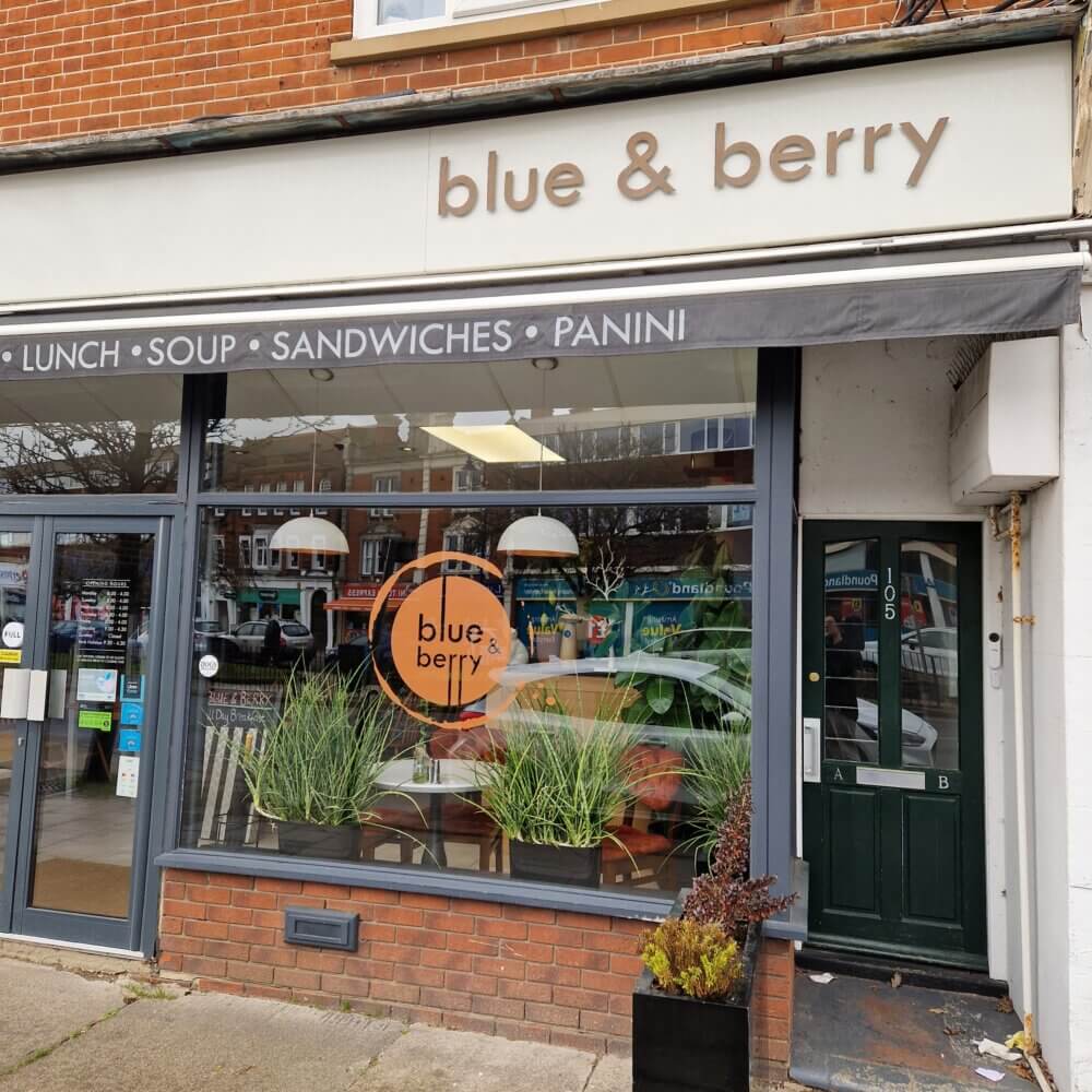 A café named "blue & berry" with a grey awning advertising lunch, soup, sandwiches, and panini. - Home Instead
