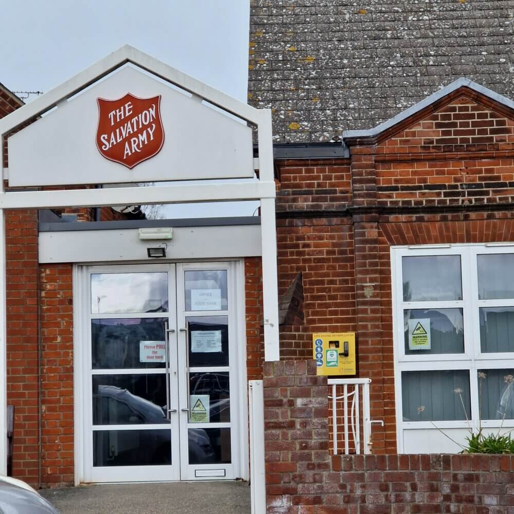 Exterior of a Salvation Army building with a white sign, brick walls, and glass entrance doors. - Home Instead