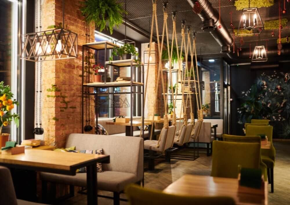 Cozy café with wooden tables, green and gray seating, hanging plants, brick walls, and swing chairs suspended from the ceiling. - Home Instead