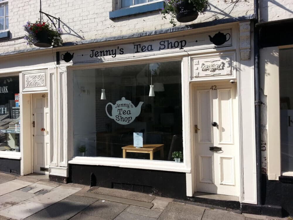 Facade of "Jenny's Tea Shop" with a large window, floral decorations, and adjacent door labeled number 42. - Home Instead
