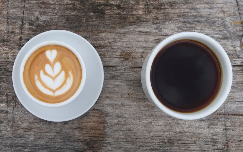 A latte with foam art and a cup of black coffee on a rustic wooden table. - Home Instead