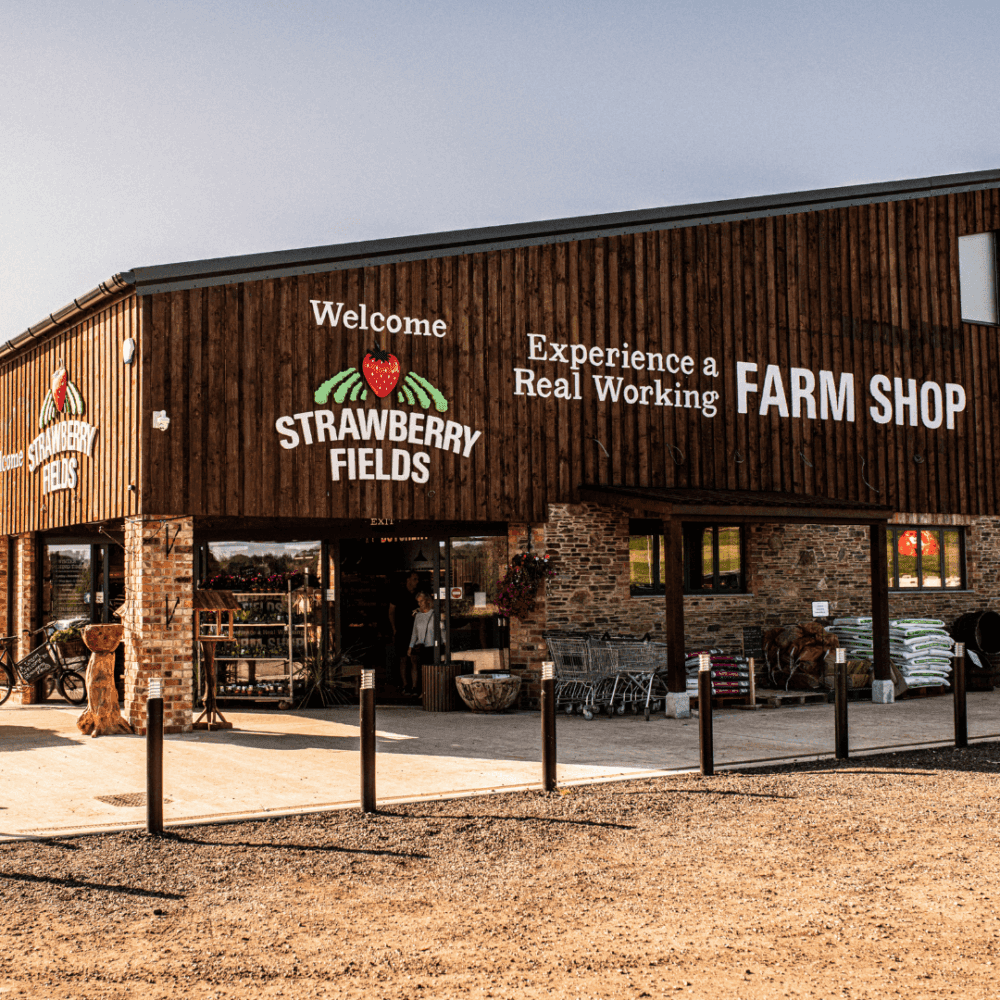 Exterior of Strawberry Fields farm shop with signage and entrance, featuring wooden architecture and outdoor displays. - Home Instead