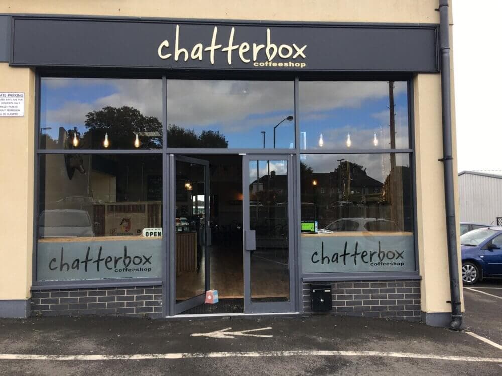 Storefront of Chatterbox Coffee Shop with large glass windows and doors, and an "Open" sign displayed. - Home Instead