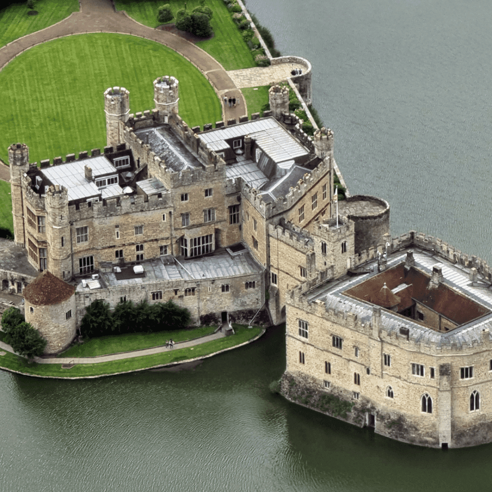 Aerial view of Leeds Castle surrounded by a moat, showcasing its medieval architecture and lush green lawns. - Home Instead