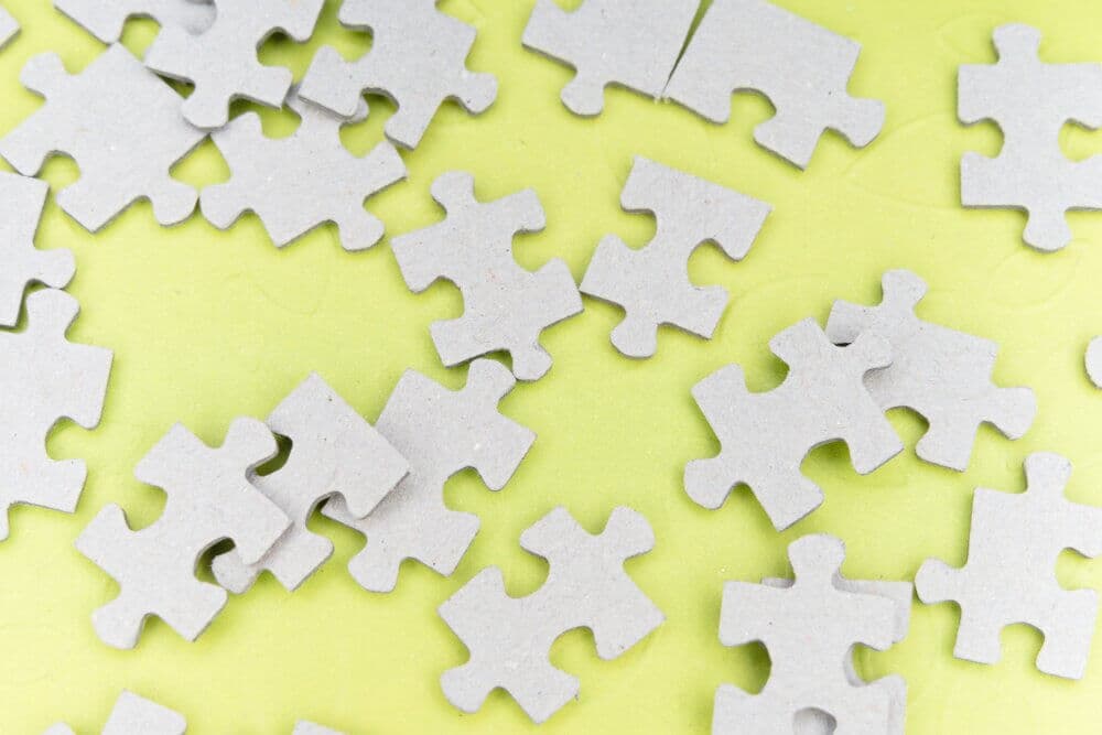 Scattered gray puzzle pieces on a bright yellow surface. - Home Instead