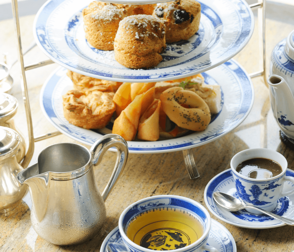 Three-tiered tray with assorted pastries and scones, blue and white china, teapot, how water jug, and cups with coffee and tea. - Home Instead