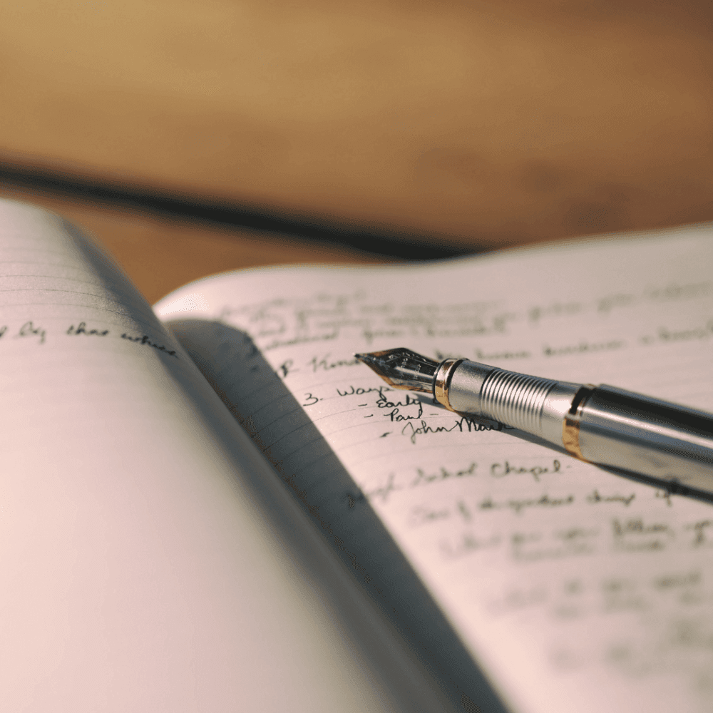 An open notebook with cursive writing and a silver fountain pen resting on the page. - Home Instead