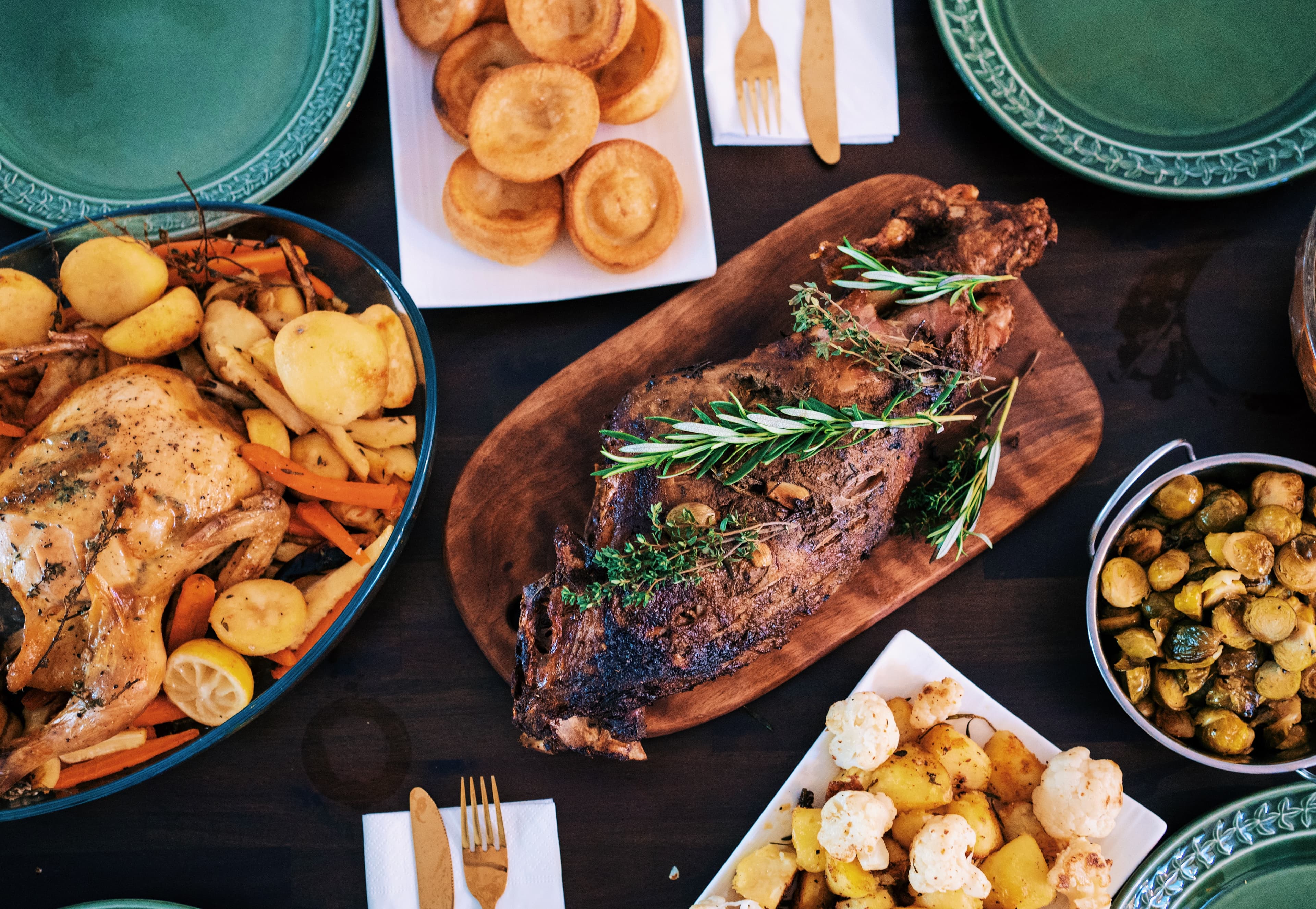 A table set with roasted meat, chicken with potatoes and vegetables, a bowl of Brussels sprouts, and green plates. - Home Instead