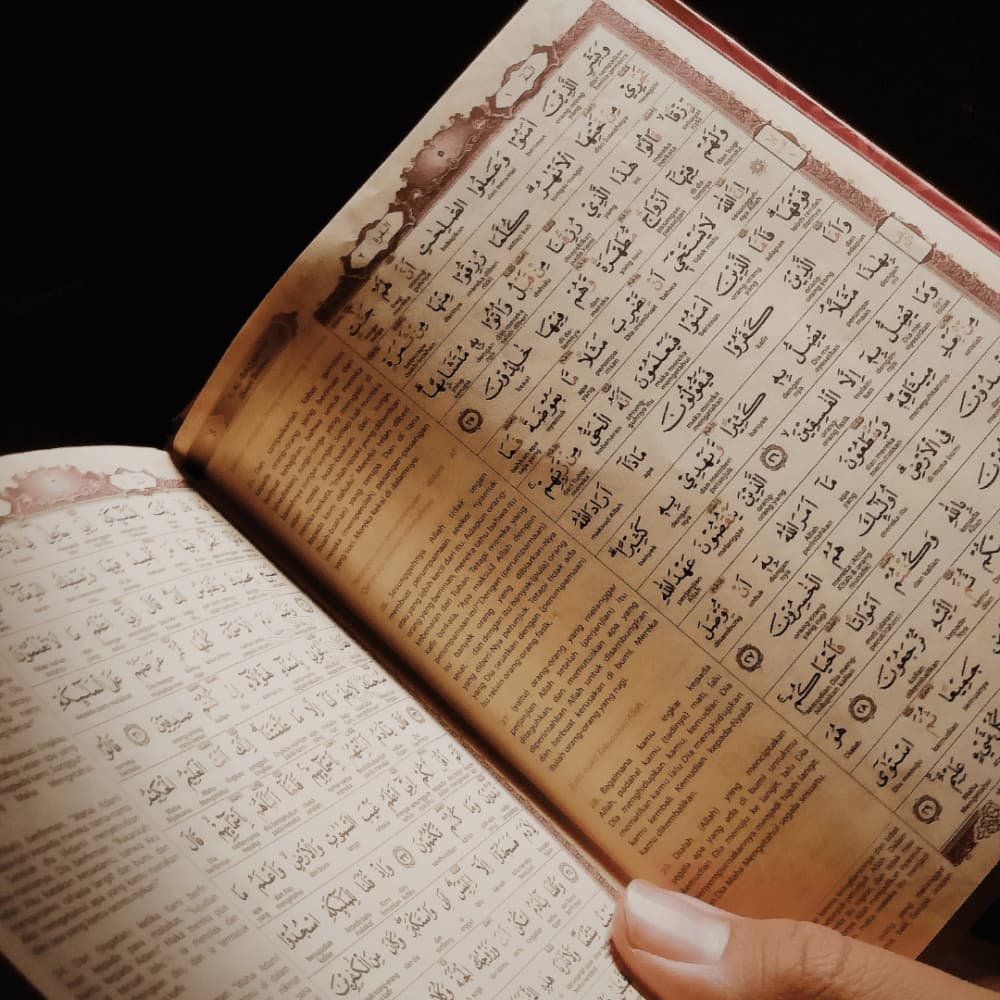 A hand holding an open book with Arabic text on its pages. - Home Instead