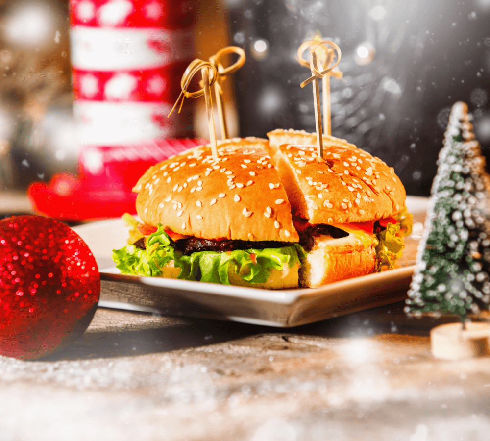 A festive burger with lettuce, cheese, and tomato on a sesame bun, served on a plate with holiday decorations. - Home Instead