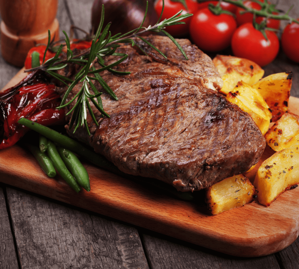 Grilled steak with rosemary, roasted potatoes, green beans, and cherry tomatoes on a wooden platter. - Home Instead