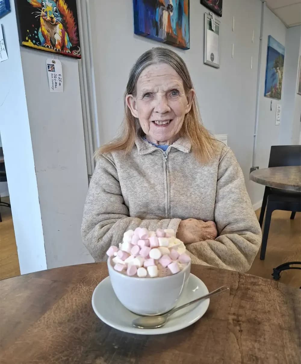 Home Instead Ascot client Jean sitting enjoying a hot chocolate with marshmallows