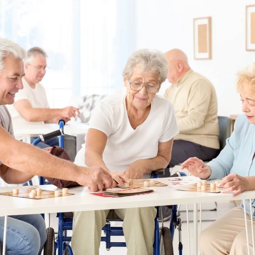 Elderly people playing board games and socializing in a bright, communal seating area. - Home Instead