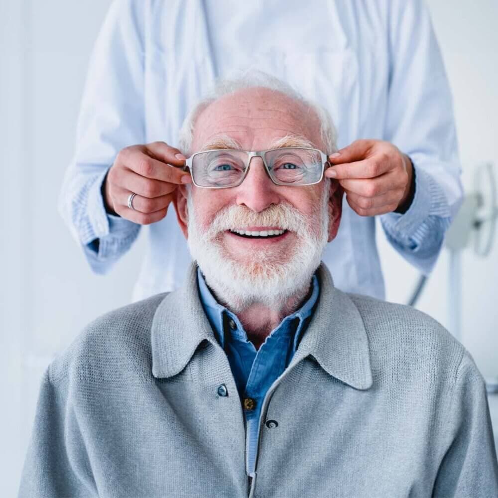 senior man smiling with new glasses being placed on his face