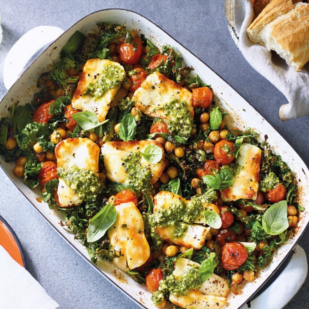 A baked dish of halloumi, chickpeas, kale, cherry tomatoes, and pesto, garnished with fresh basil leaves. - Home Instead Renfrewshire and Barrhead home care - Meal preparation.