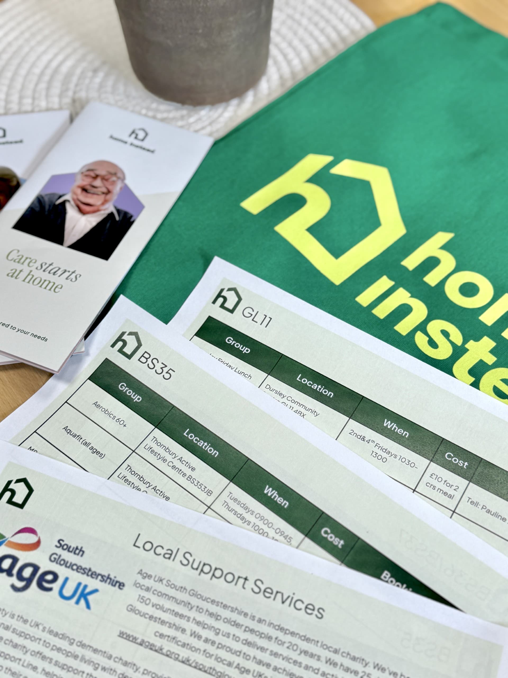 Home Instead brochures, lists of support services, and a green Home Instead bag on a table. - Home Instead