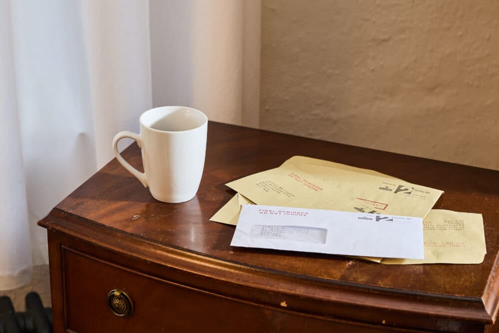 White mug and assorted post on a wooden table next to a curtain and beige wall. - Home Instead