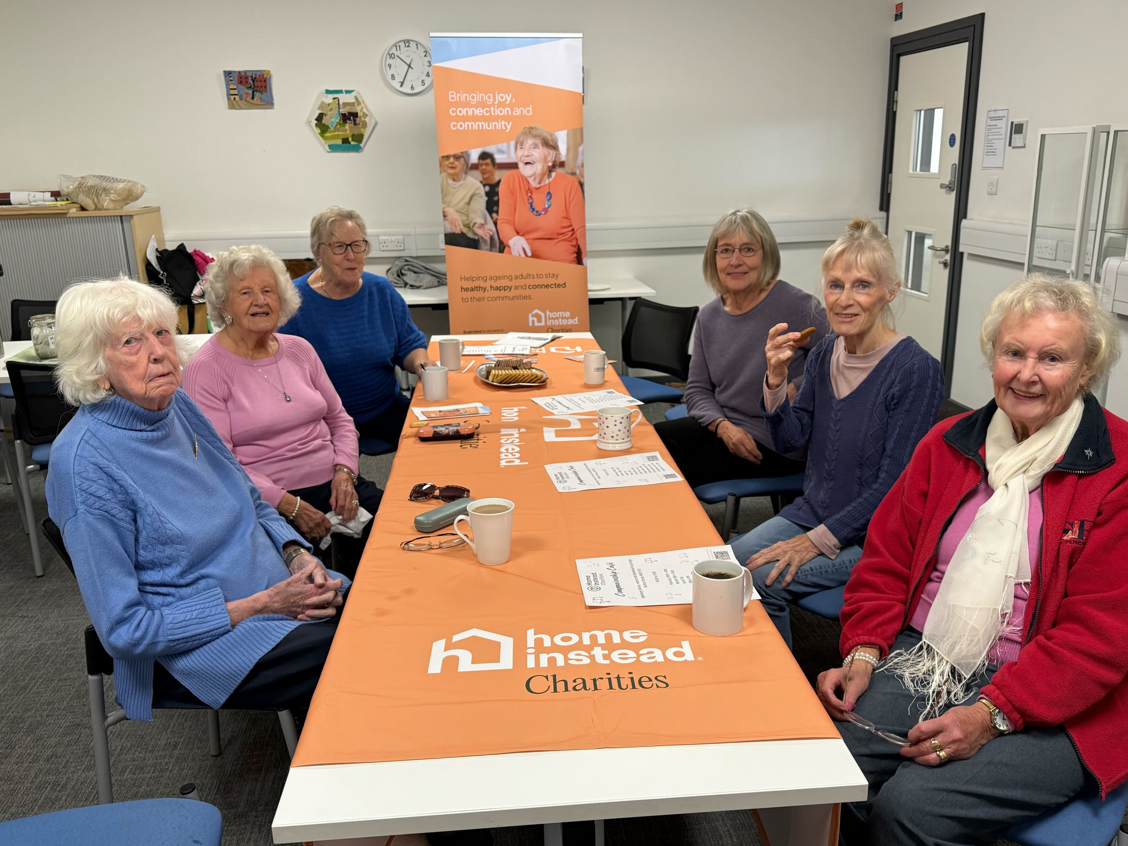 Group of smiling women around a Home Instead Charities branded table.