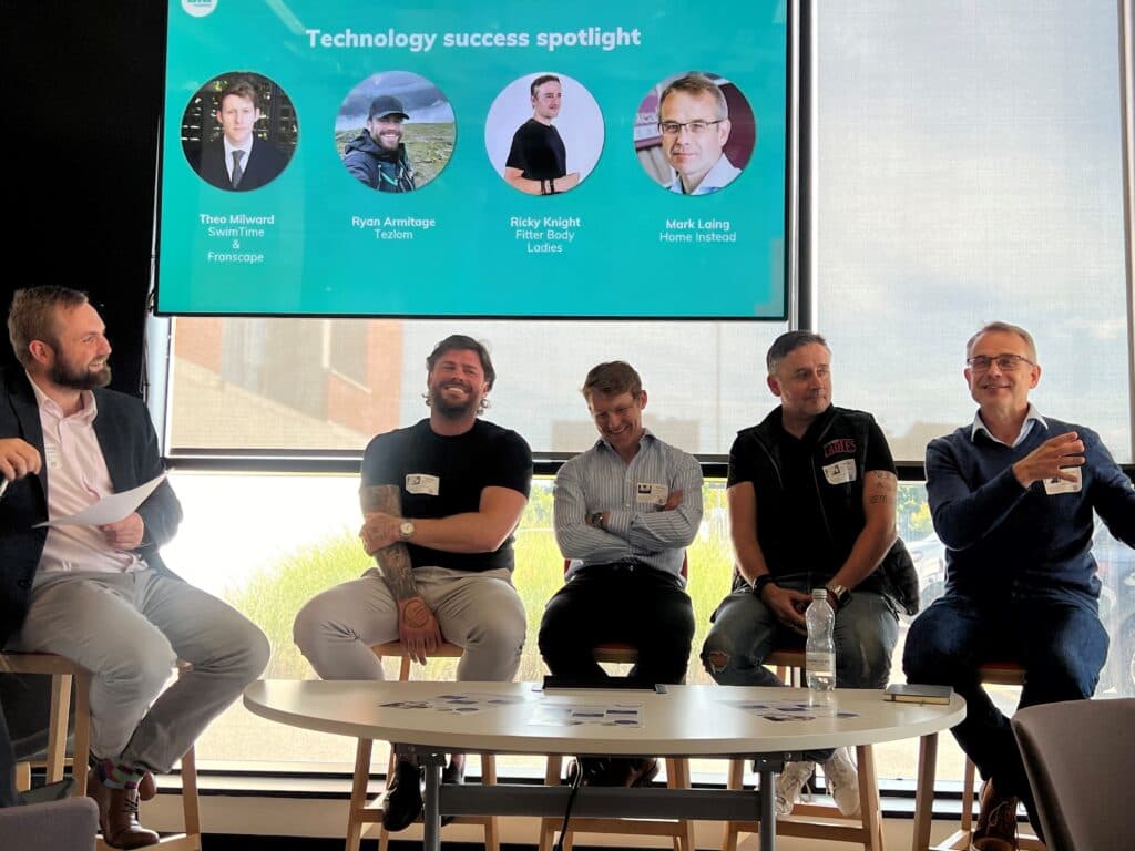 Five men sit on stools in front of a screen displaying "Technology success spotlight" and their names. - Home Instead