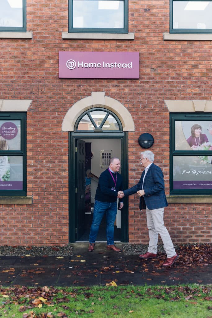 Two men shake hands outside the entrance of a Home Instead office building. - Home Instead