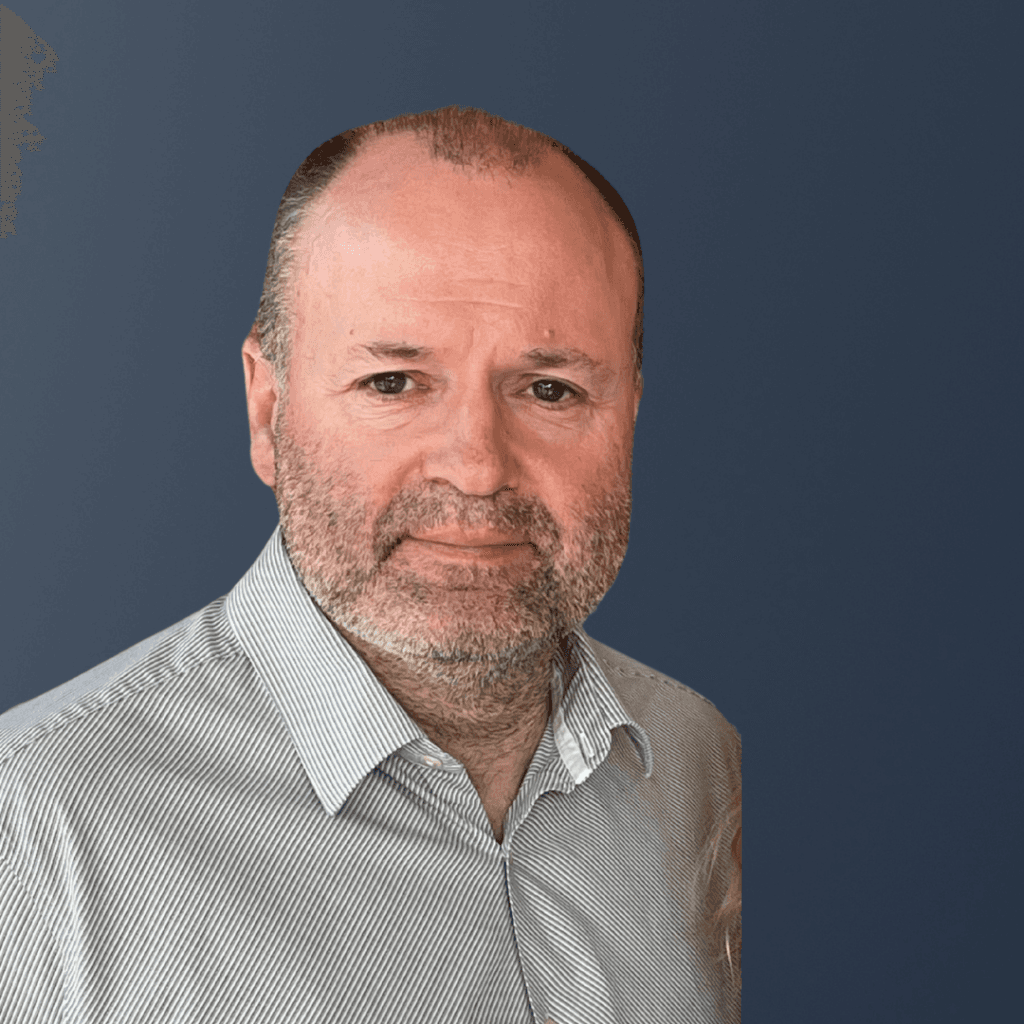 A middle-aged Home Instead franchisee with a beard, wearing a striped shirt, posed against a plain dark blue background. - Home Instead