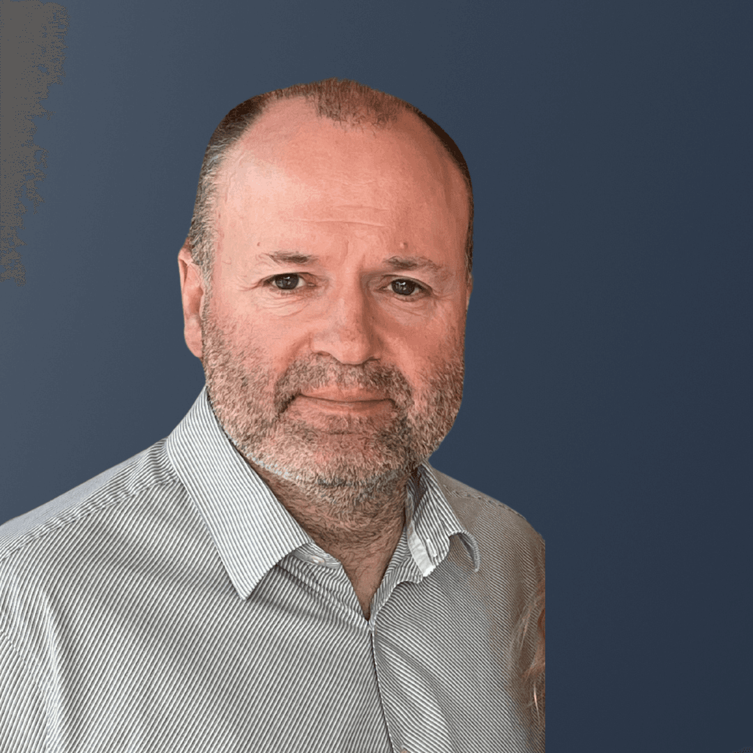A middle-aged Home Instead franchisee with a beard, wearing a striped shirt, posed against a plain dark blue background. - Home Instead