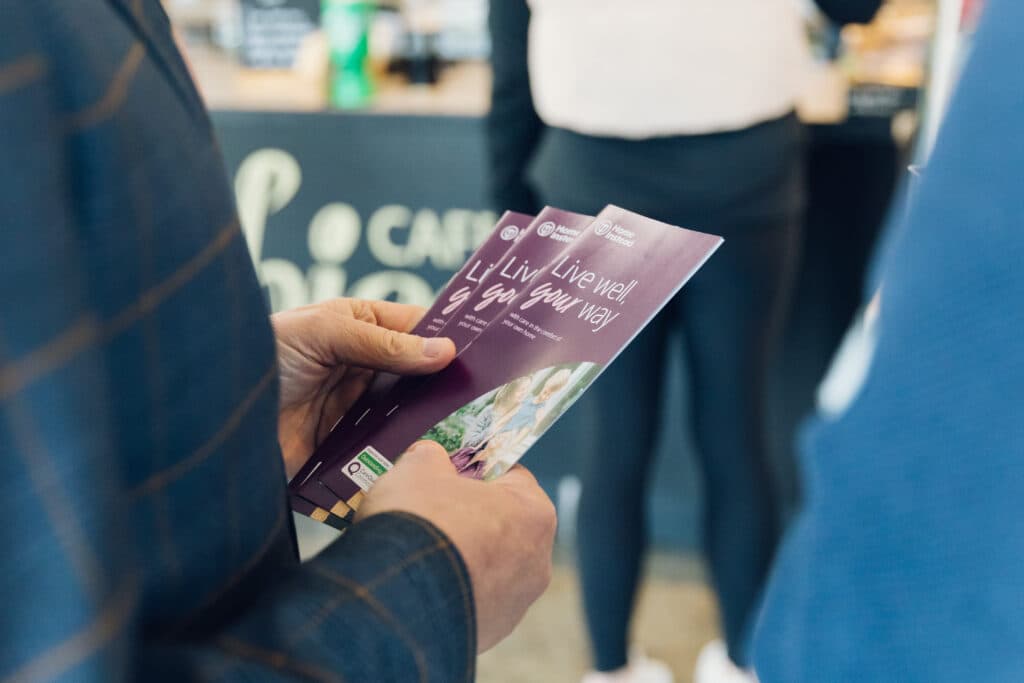 A person holds three purple leaflets that read, "Live well, your way" in a casual indoor setting. - Home Instead