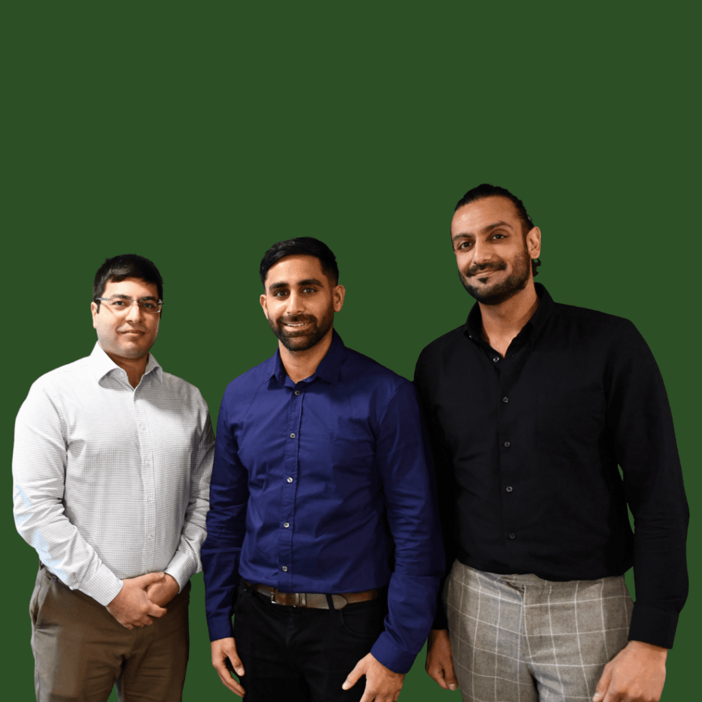 Three men standing side by side, posing and smiling in front of a plain green background. - Home Instead