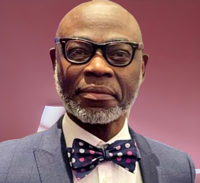 An older man in spectacles and a blue suit with a spotted bow tie, against a pink background. - Home Instead