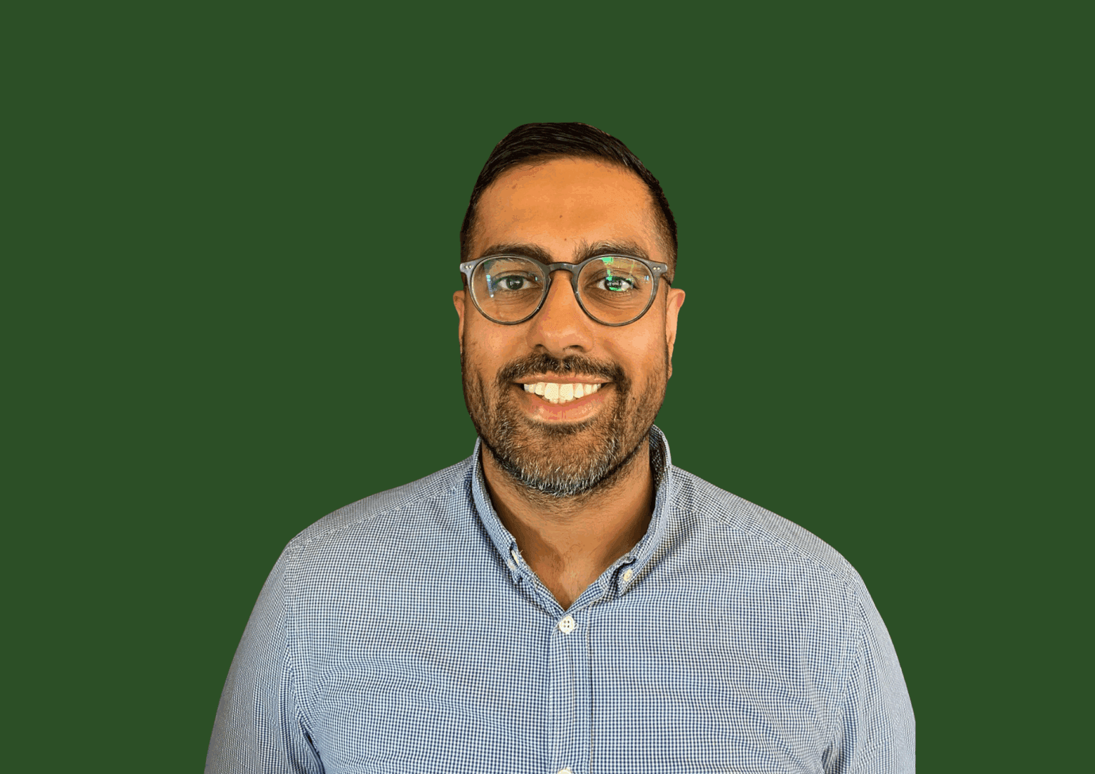 A man wearing glasses and a blue shirt smiles in front of a solid green background. - Home Instead