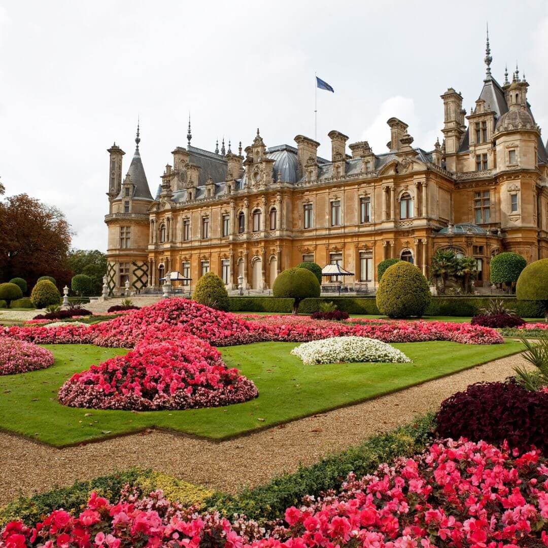 Ornate historic mansion with manicured gardens featuring vibrant pink and white flower beds in the foreground. - Home Instead
