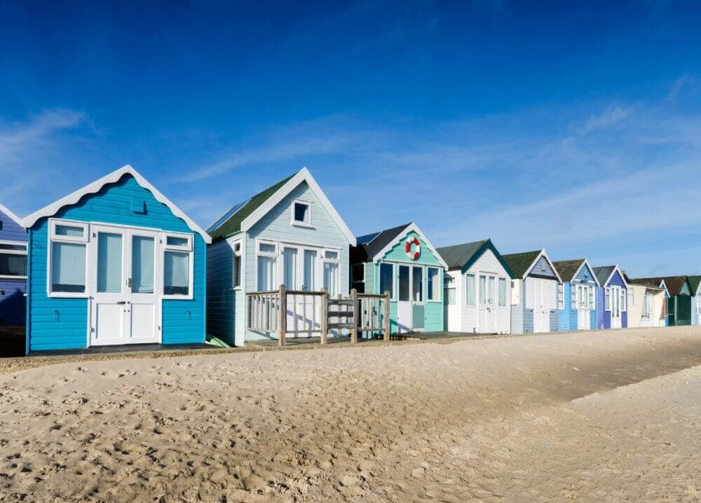 A row of colourful beach huts on a sandy shore under a clear blue sky. - Home Instead Bournemouth & Christchurch