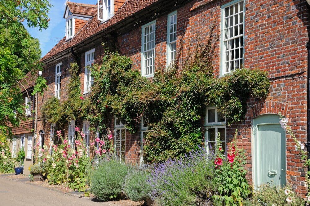 Charming brick houses with tall windows, green doors, and colorful flowers lining the front on a sunny day. - Home Instead