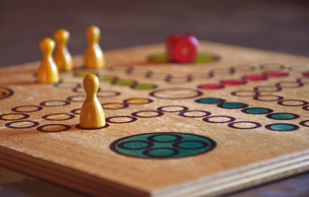 Close-up of a board game with colored pawn pieces and a red die. The board has circular patterns and green marks. - Home Instead
