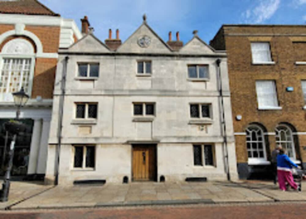 A historic white stone building with two dormer windows, a wooden door, and adjoining brick buildings on a sunny day. - Home Instead
