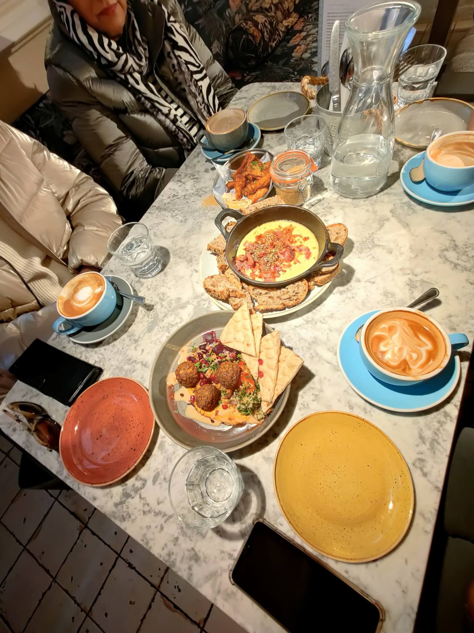 A table with various dishes including hummus, falafel, and drinks. Two people sit on either side of the table. - Home Instead