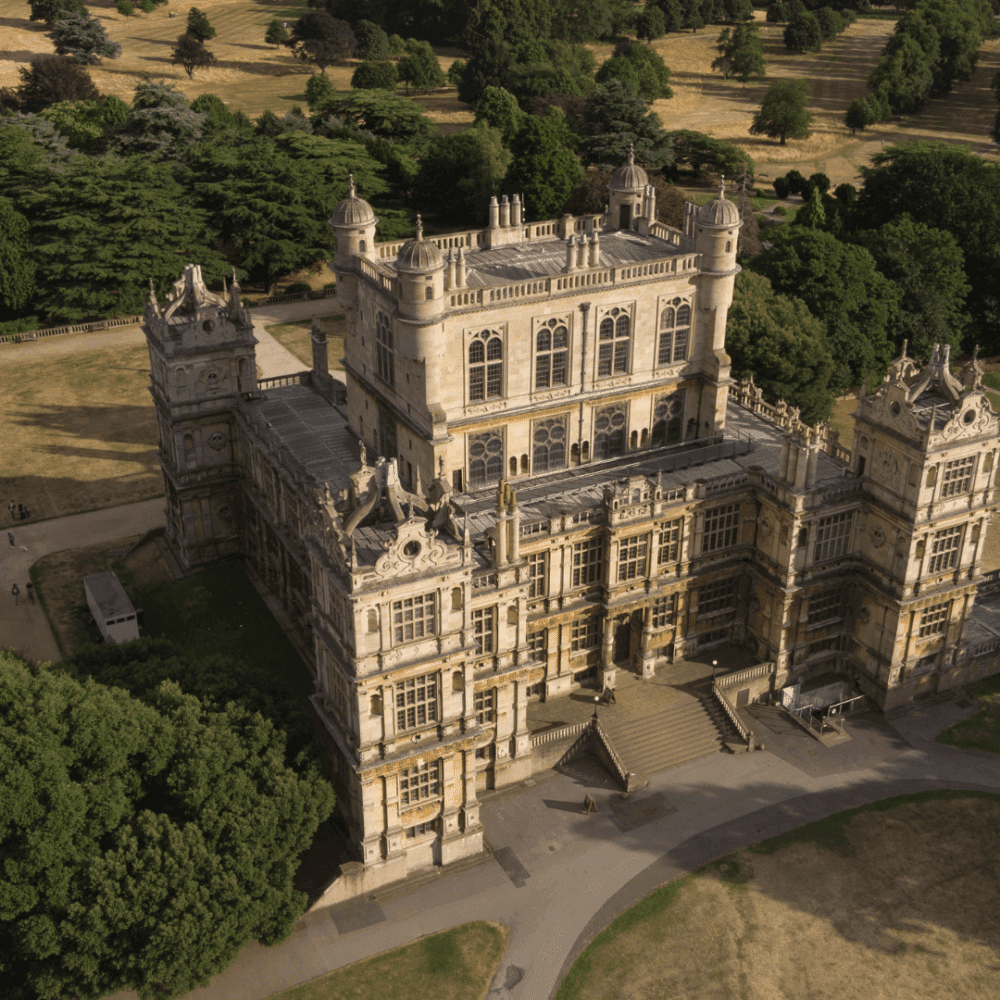 Aerial view of a grand historic mansion with ornate architecture, surrounded by trees and greenery on a sunny day. - Home Instead