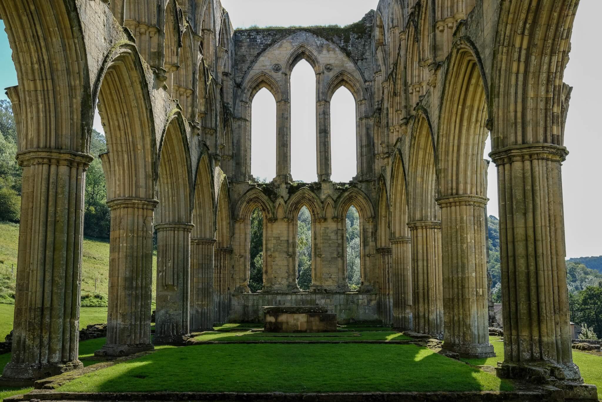 Interior view of a historic stone cathedral ruin with pointed arches, tall windows, and a grassy floor. - Home Instead